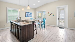 Una cocina con una isla central, armarios de madera, una zona de comedor con sillas y una puerta que da al exterior.
