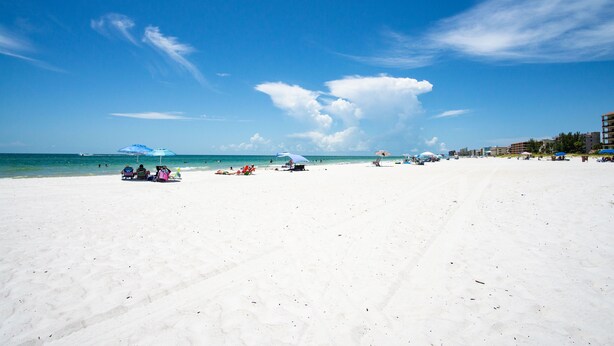 Una extensa playa de arena con cielo azul despejado y algunas nubes.