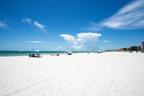 Una extensa playa de arena con cielo azul despejado y algunas nubes.