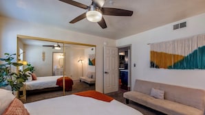 Ein Hotelzimmer mit Bett, Sofa, Deckenventilator, Spiegel und einer Wand mit Vorhang.
