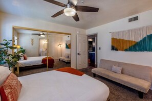Une chambre d’hôtel avec un lit, un canapé, un ventilateur de plafond, un miroir et un mur sur lequel est accroché un rideau.