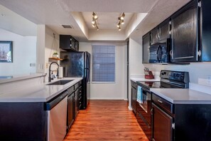 Une cuisine moderne avec des meubles noirs, des appareils en acier inoxydable et un plancher en bois.