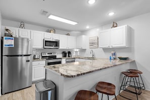 A modern kitchen with white cabinets, stainless steel appliances, a marble countertop, and bar stools.