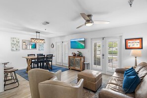 A living room with a brown leather couch, a dining area with a wooden table and chairs, and a ceiling fan.