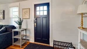 Een woonkamer met een donkere deur, een witte muur, een blauwe bank, een kleine tafel met een plant en een lamp.