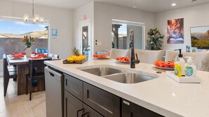 Una cocina moderna con electrodomésticos de acero inoxidable, una isla grande con pileta y un comedor con mesa y sillas de madera.