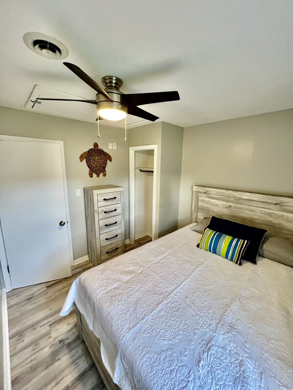 A bedroom with a bed, a ceiling fan, a dresser, and a door.