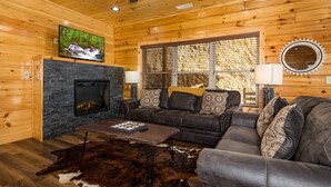 L’intérieur d’un chalet chaleureux, avec une cheminée, un canapé en cuir et un téléviseur fixé au mur, juste au-dessus de la cheminée.