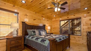 Une chambre dans une cabane en bois, avec un lit, des tables de chevet et un ventilateur de plafond.