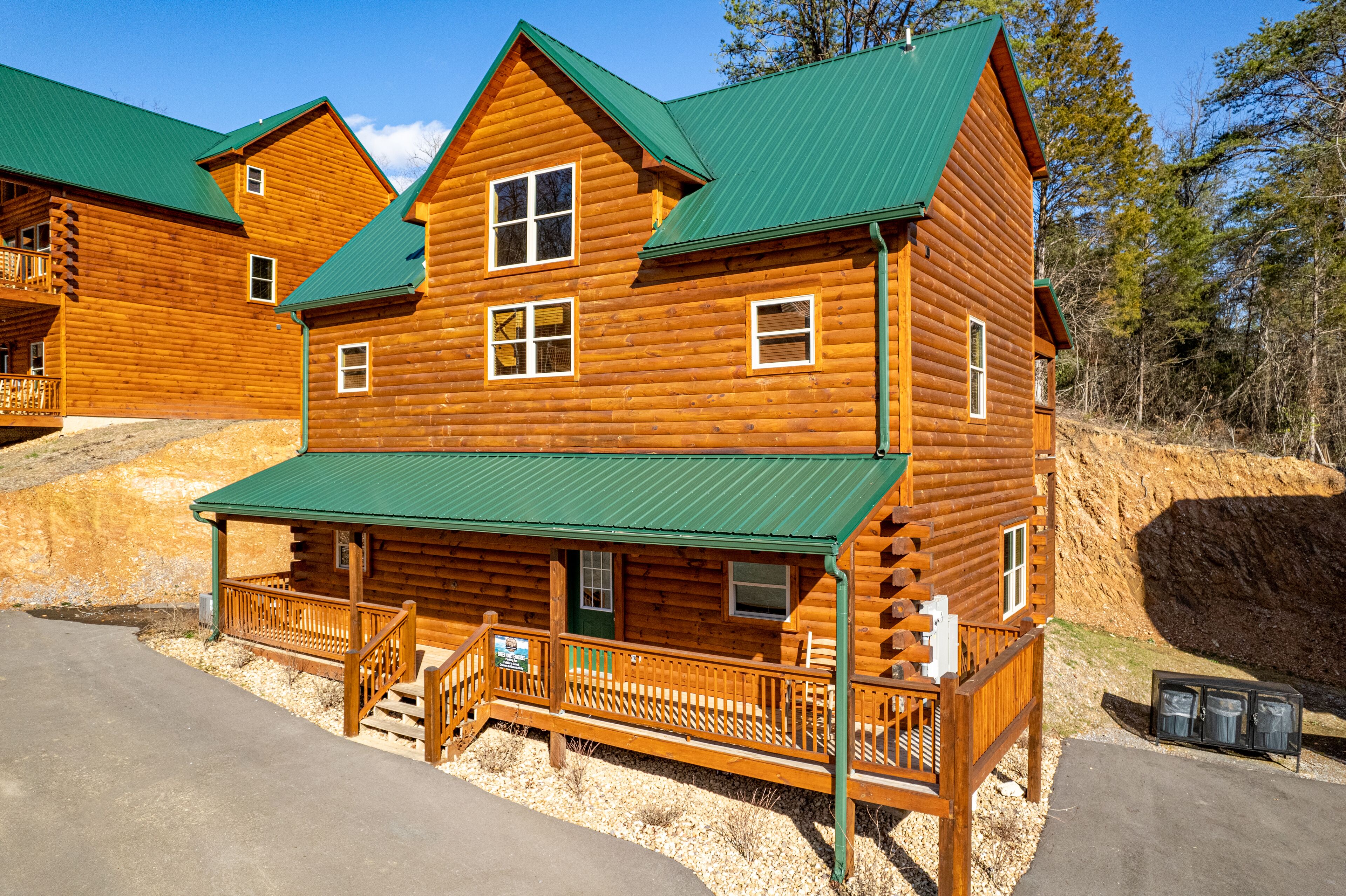 A large log cabin with a green roof, multiple windows, and a porch with a railing.