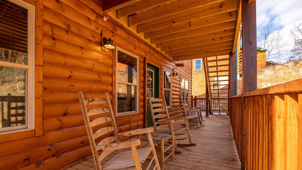 Une cabane en bois avec une véranda, des chaises en bois et une échelle.