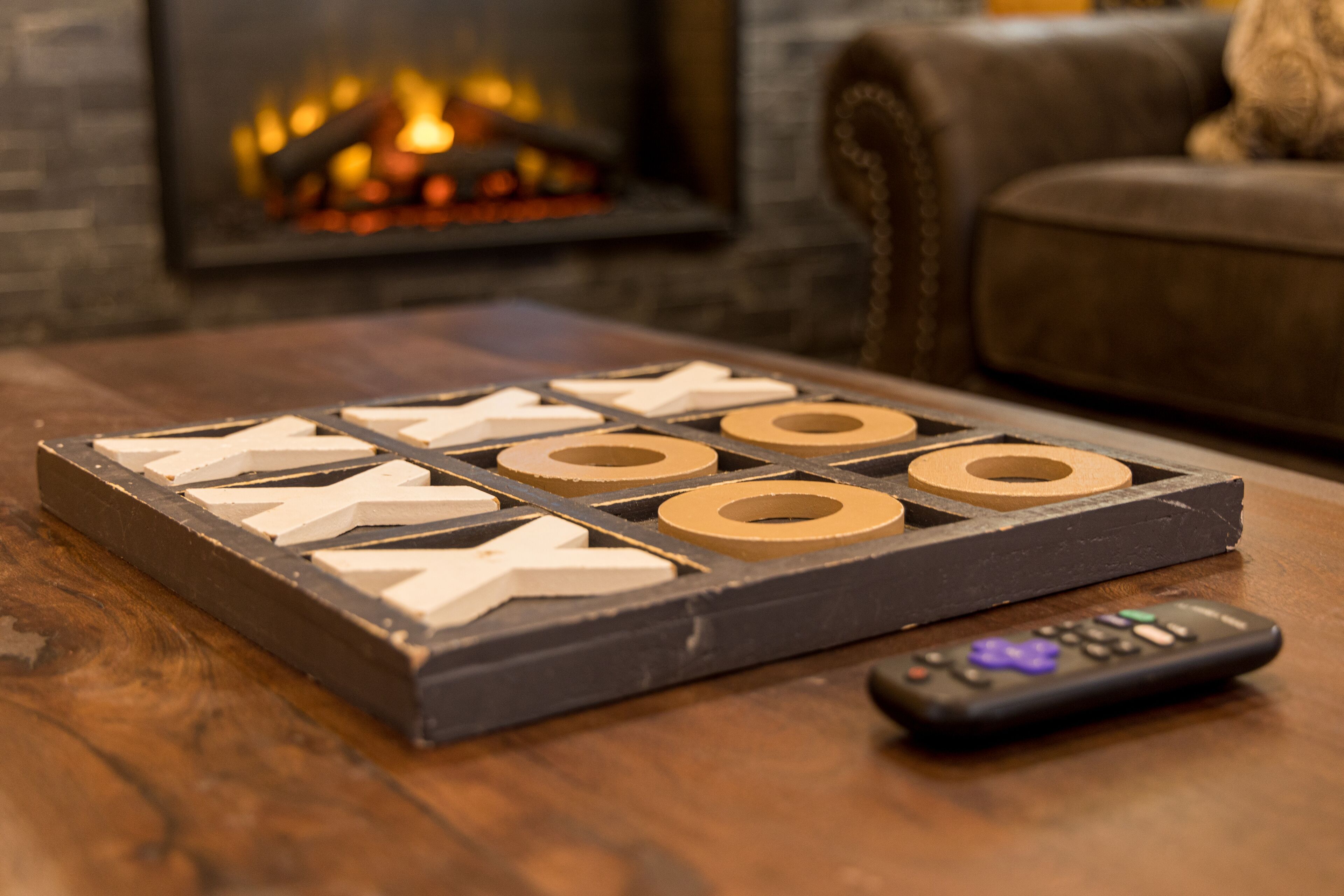 A wooden board game with letter tiles on a table, a remote control, and a fireplace in the background.