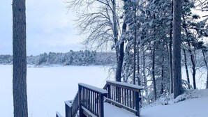 A snow-covered deck with a wooden railing leading down to a snowy path. - Family Lakefront Cabin! Hot Tub, Arcades & Dock (Wautoma)