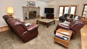 Una sala de estar con sofás de cuero, chimenea, televisor y un amplio ventanal.