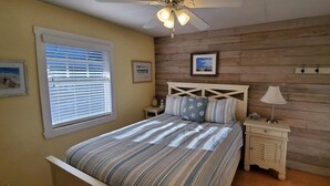 Un dormitorio con una cama, una mesita de noche, una lámpara, un ventilador de techo y paneles de madera en las paredes.