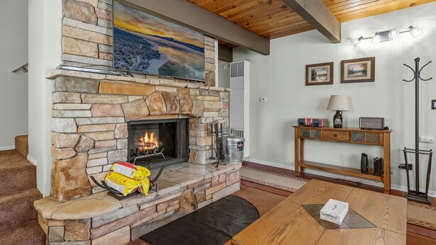 A stone fireplace with a TV above it, a wooden ceiling, and a painting of a sunset. - KC's Haven - Relax with the whole family at this peaceful cabin. Smart TV, Fenced Yard (Sugarloaf)
