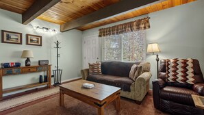 A cozy living room with a wooden ceiling, a sofa, a leather armchair, a coffee table, and a lamp. - KC's Haven - Relax with the whole family at this peaceful cabin. Smart TV, Fenced Yard (Sugarloaf)