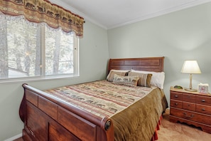 Un dormitorio con una cama de madera, una mesita de noche con lámpara y una ventana con cortinas estampadas.