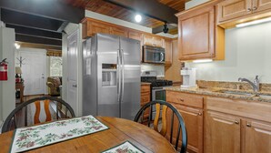 A kitchen with wooden cabinets, stainless steel appliances, and a dining table with a floral tablecloth. - KC's Haven - Relax with the whole family at this peaceful cabin. Smart TV, Fenced Yard (Sugarloaf)