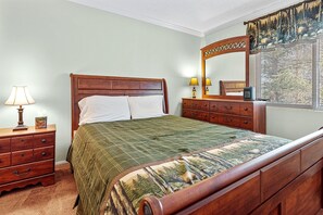 Un dormitorio con una cama de madera, una mesita de noche con lámpara, un aparador y un espejo.