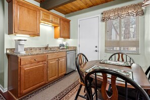 Una cocina con armarios de madera, cafetera, lavaplatos y una mesa de comedor con sillas.