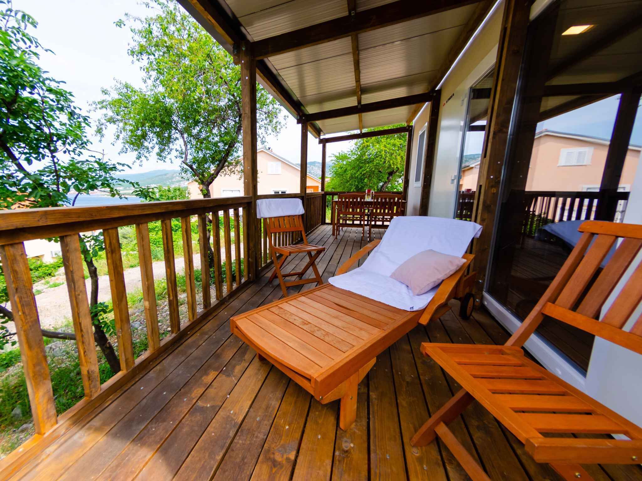 Une terrasse en bois avec des chaises longues et une table, donnant sur un jardin et un bâtiment.