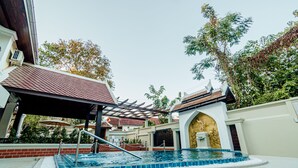 A swimming pool with a tiled deck, a covered area with a red roof, and a building with a gold-colored entrance. - Lux hotel Luang Prabang (Luang Prabang)