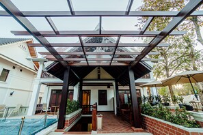 A covered outdoor area with a pool, wooden benches, and a brick wall.