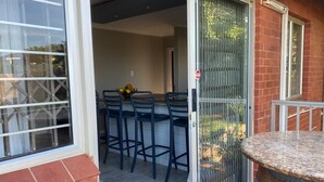 Eine Terrasse mit Tisch und Stühlen, einer Schiebetür und einer Backsteinmauer.