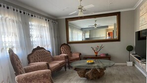 Ein Wohnzimmer mit einem runden Glastisch, zwei Sesseln, einem Sofa, einem großen Spiegel und einem Fernseher.