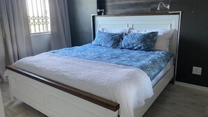 Ein Schlafzimmer mit einem weißen Bett, blau gemusterten Betttextilien und einem Fenster mit Vorhängen.