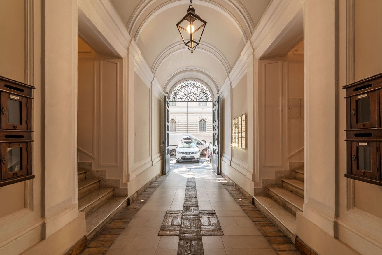 A hallway with a stone floor, white walls, and a large arched window at the end.