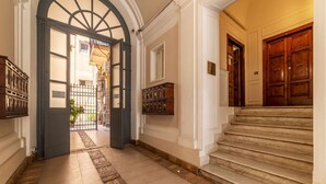 A grand hallway with a marble staircase, wooden doors, and a view into a courtyard. - Castro Pretorio 3 - FromHometoRome (Roma)
