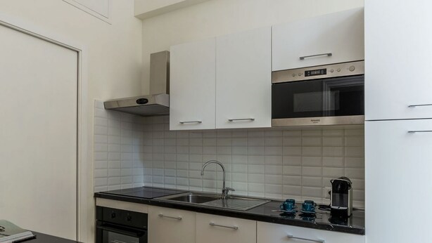 A modern kitchen with white cabinets, a stainless steel range hood, a microwave, and a coffee maker. - Castro Pretorio 3 - FromHometoRome (Roma)