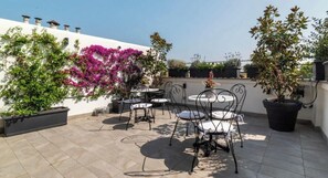 An outdoor patio with a round table and chairs, surrounded by potted plants and a white wall.