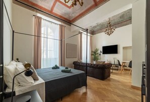 A modern hotel room with a bed, a sofa, a TV, and a dining area.