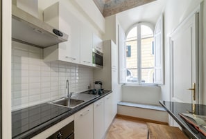 Una cocina con armarios blancos, encimera negra y ventana con vista a la calle.