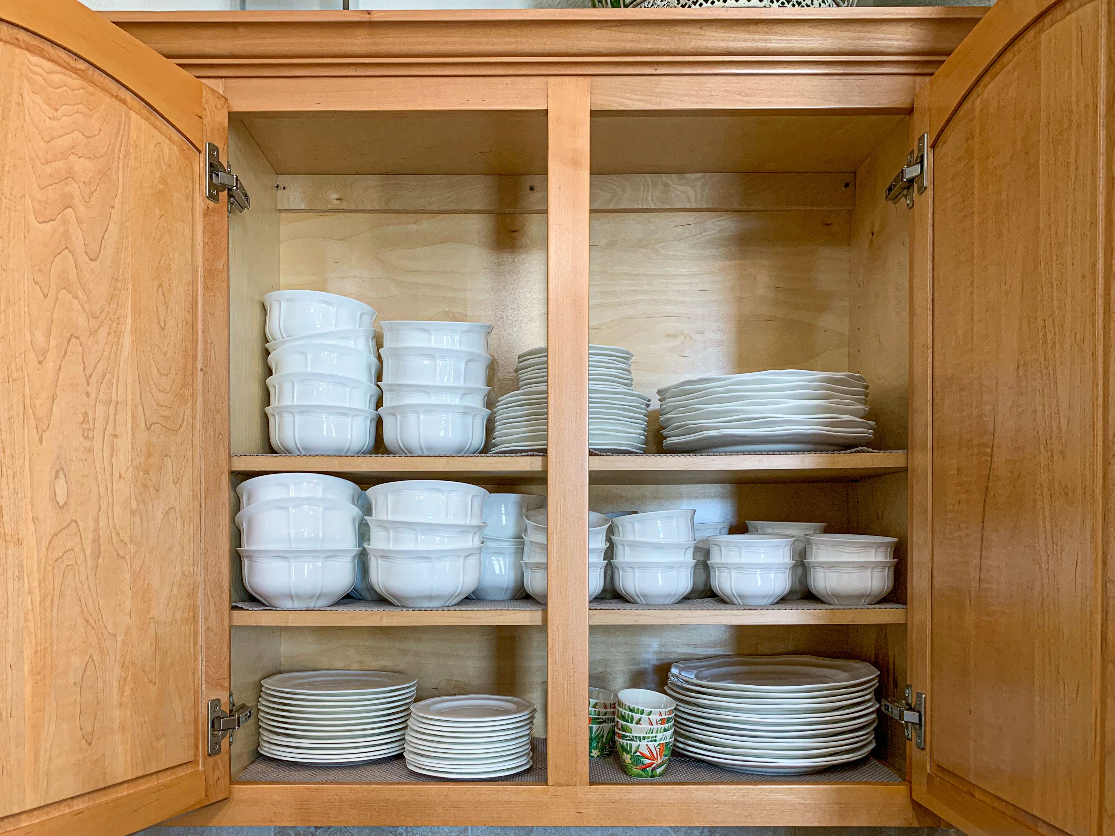Un meuble en bois doté de plusieurs étagères, contenant des bols blancs, des assiettes et quelques tasses à motifs.
