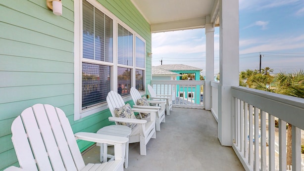 A porch with white Adirondack chairs and a green building with white trim. - Beautiful Home in Gated Village Walk, 2 Shared Heated Pools, Pets Allowed, Garage Access (Port Aransas)