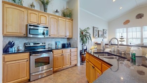 A kitchen with wooden cabinets, stainless steel appliances, and a large island with a sink. - Beautiful Home in Gated Village Walk, 2 Shared Heated Pools, Pets Allowed, Garage Access (Port Aransas)