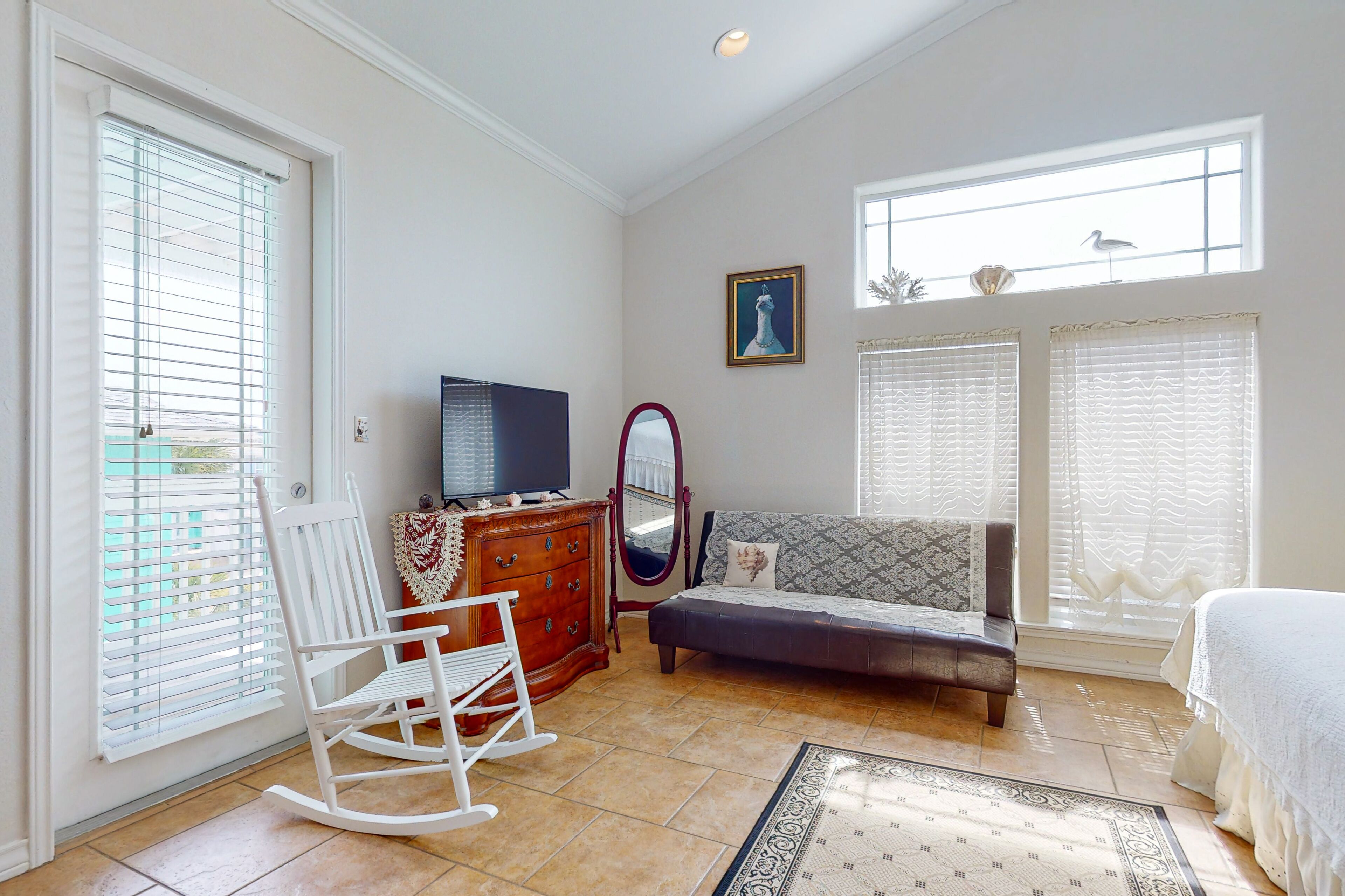 A bedroom with a bed, a dresser, a television, a rocking chair, and a window with blinds.