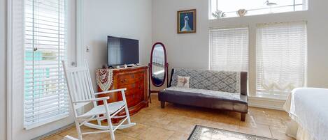 A bedroom with a bed, a dresser, a television, a rocking chair, and a window with blinds.