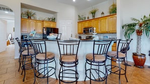 A kitchen with wooden cabinets, a central island with bar stools, and various plants. - Beautiful Home in Gated Village Walk, 2 Shared Heated Pools, Pets Allowed, Garage Access (Port Aransas)