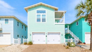 A two-story building with a front garage, a balcony, and a staircase leading to a second level. - Beautiful Home in Gated Village Walk, 2 Shared Heated Pools, Pets Allowed, Garage Access (Port Aransas)