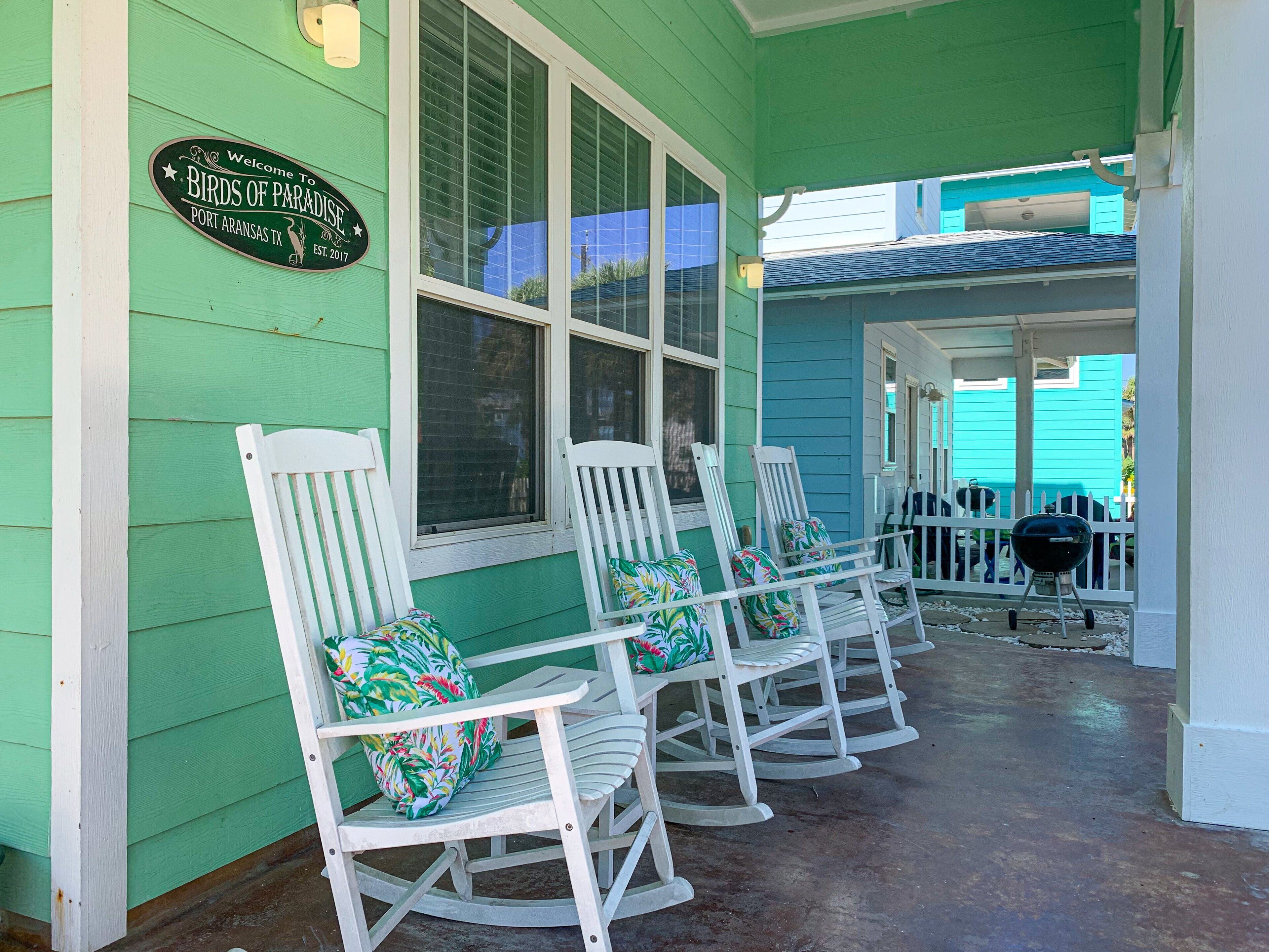 A porch with white rocking chairs and a sign reading "Welcome to Birds of Paradise, Port Aransas, TX."