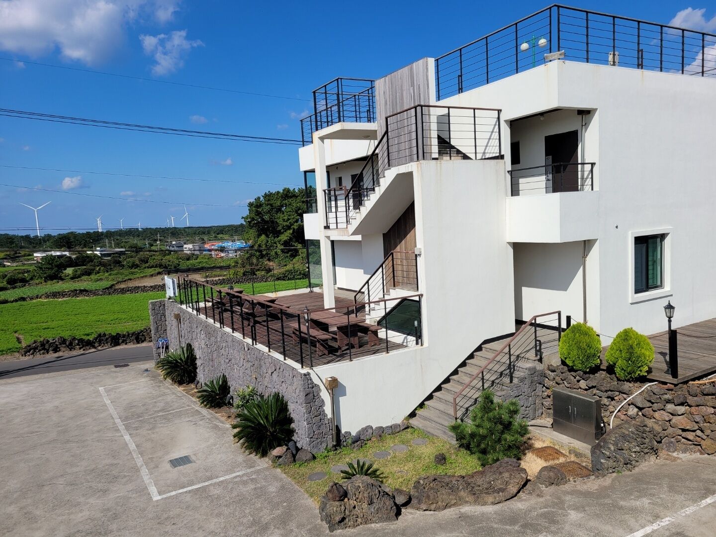 A modern two-story building with a balcony, a staircase, and a stone retaining wall.