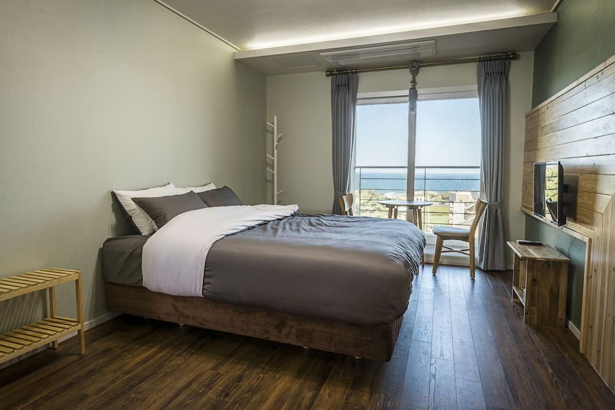 A bedroom with a bed, a TV, a small table, and a chair.