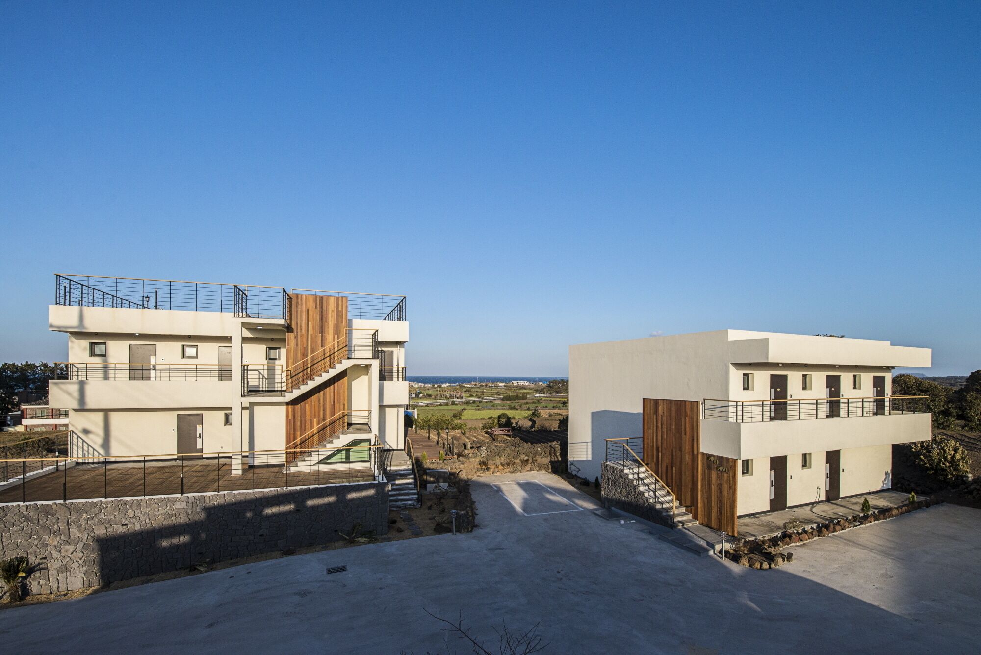 A modern two-story building with a flat roof, a staircase, and a view of the landscape.