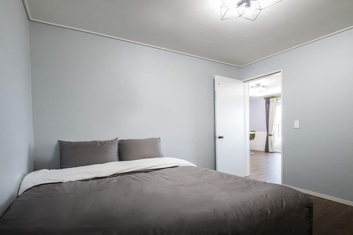 A bedroom with a bed, a door leading to another room, and a ceiling light fixture.