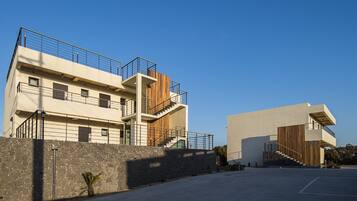 A modern multi-story building with balconies, a stone wall, and a parking area.